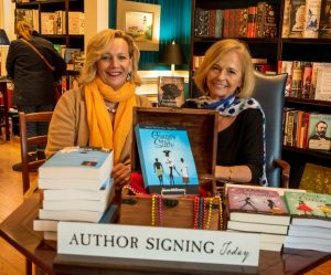 Picture of Diana McDonough at book signing and launch party sitting in front of books.